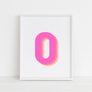 以下が含まれることがあります： 中央にピンクとピーチの重ねられた文字「O」が描かれた白い額縁入りプリント