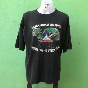 May include: Black t-shirt featuring a graphic of a person playing a guitar in front of a globe. The text "International Rectifier Vision 1994-95 World Tour" is printed on the shirt.