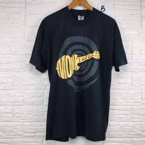 May include: Black t-shirt with a graphic of a guitar shaped like the word "MONKEES" in yellow and orange letters on a black and gray spiral background.