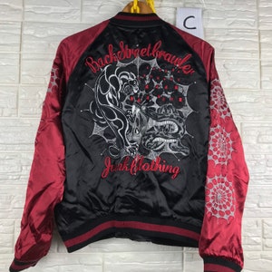 Puede incluir: Chaqueta bomber de satén negro con mangas de satén rojo. La parte posterior presenta un diseño bordado de una pantera y una serpiente en una telaraña con el texto "Back Street Brawler Junk Clothing".