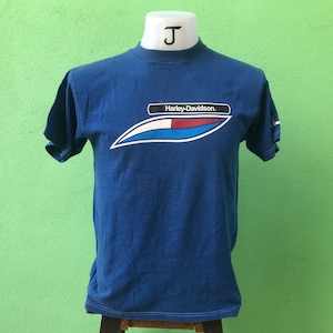 May include: Blue short-sleeved t-shirt with a white, red, and blue graphic of a stylized wave and the text "Harley-Davidson."