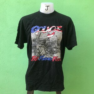 Puede incluir: Camiseta negra con un gráfico de una bandera estadounidense roja, blanca y azul con la palabra "GRICE" escrita en letras blancas. El texto "Fast Furious Free" está escrito debajo de la bandera.