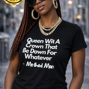 May include: A black short-sleeved t-shirt featuring white text that reads: Queen Wit A Crown That Be Down For Whatever - Method Man. The shirt has a crew neckline and a fitted cut, displayed with gold-toned hoop earrings and a layered gold chain necklace.