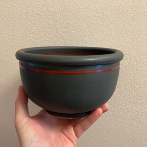 May include: A dark grey ceramic planter with a red stripe around the rim.