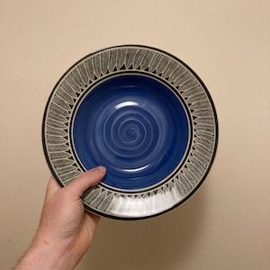 May include: A blue ceramic bowl with a white and black feather design around the rim. The bowl has a blue swirl pattern on the inside.
