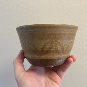 Könnte beinhalten: Eine braune Keramikschüssel mit hellbraunem Überzug und einem Blattmotiv am Rand.