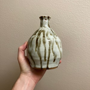 Op de afbeelding: Een witte keramische vaas met bruine glazuur, met een druppelvormig patroon. De vaas heeft een rond lichaam en een smalle hals.