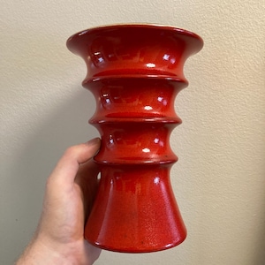 Könnte beinhalten: Eine leuchtend rote Keramikvase mit glänzendem Finish. Die Vase hat ein einzigartiges, gestapeltes Design mit ausgestelltem Boden und breiterem Oberteil. Die handgehaltene Vase ist etwa 20 cm hoch, perfekt für die Inneneinrichtung.