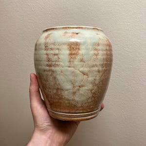 May include: A ceramic vase with a light brown and white glaze. The vase has a rounded body and a slightly flared lip.