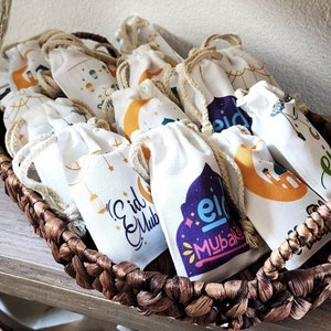 May include: A wicker basket filled with small white fabric bags with colorful designs and the text "Eid Mubarak".