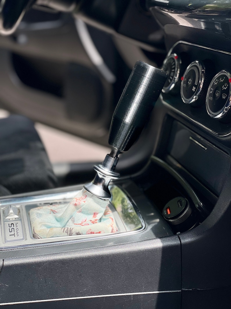 Puede incluir: Primer plano de la palanca de cambios de un coche con una perilla de cambio negra y una funda de palanca de cambios con estampado. La palanca de cambios est&aacute; etiquetada como "SST" y "Top Clutch".
