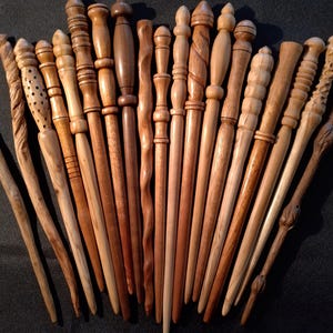 May include: A collection of handcrafted wooden wands in various shades of brown. Each wand has a unique design, including carved details, spiral patterns, and textured surfaces. The wands vary in length and thickness, showcasing a range of woodworking techniques.