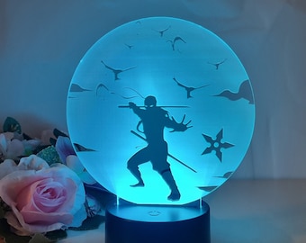 May include: A blue LED night light with a silhouette of a ninja holding a sword and throwing a star. The ninja is surrounded by birds in flight.