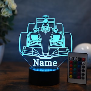 May include: A blue and white 3D printed night light shaped like a race car with the word "Name" underneath. The light is on a black base and comes with a remote control with multiple color options.
