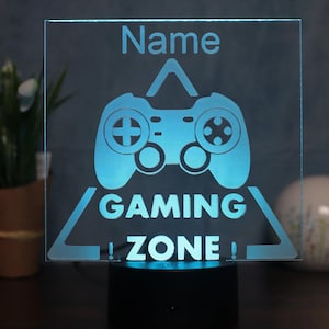 Könnte beinhalten: Ein blaues beleuchtetes Schild mit einem weißen Gamecontroller und dem Text "Name GAMING ZONE!"