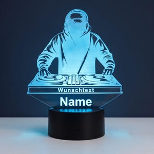 Könnte beinhalten: Eine hellblaue LED-Lampe mit einer Acrylsilhouette eines DJs, der Kopfhörer trägt und ein Mischpult bedient. Auf der Vorderseite des Mischpults steht der Text "Wunschtext" über dem Wort "Name" in einer fetten, weißen serifenlosen Schrift.