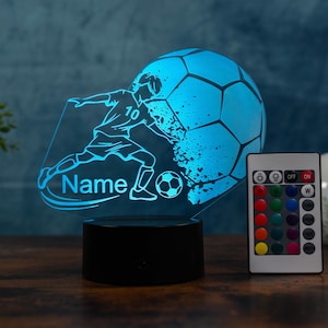 Könnte beinhalten: Blaues LED-Nachtlicht zum Thema Fußball mit einer Grafik eines Fußballspielers und eines Fußballs. Der Sockel ist schwarz, und eine Fernbedienung ist im Lieferumfang enthalten. Der Text "Name" ist auf dem Licht sichtbar.