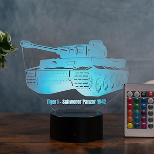 Op de afbeelding: Een blauw getinte acryl nachtlamp in de vorm van een Tiger I tank, met de tekst "Tiger I - Schwerer Panzer 1942" aan de basis. Een afstandsbediening met meerdere kleuropties staat rechts. Het licht staat op een zwarte basis.
