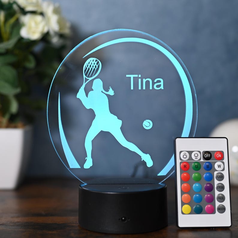 May include: A clear acrylic night light with a silhouette of a tennis player and a tennis ball. The light has a remote control with multiple color options and the name "Tina" is printed on the light.