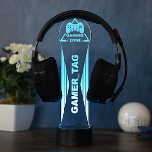 May include: A blue LED light with a black base and a black headset resting on it. The light features a gamer icon and the text "GAMING ZONE" and "GAMER_TAG".