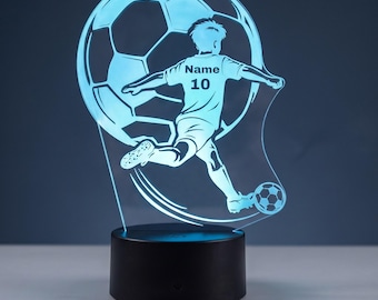 May include: A light blue LED lamp featuring an acrylic cutout of a soccer player kicking a ball. The player is positioned in front of a large soccer ball graphic. The text "Name" and "10" are printed on the player's jersey. The lamp has a black base.