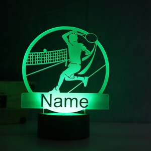Op de afbeelding: Groen LED-nachtlampje met een silhouet van een tennisspeler in een cirkel. De voet van het lampje heeft ruimte voor een naam, die "Naam" zegt.