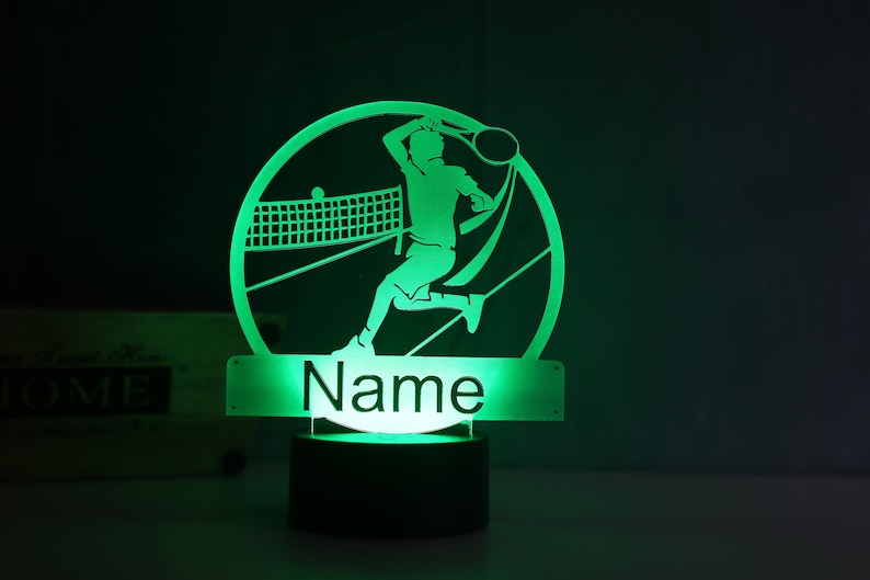 Op de afbeelding: Groen LED-nachtlampje met een silhouet van een tennisspeler in een cirkel. De voet van het lampje heeft ruimte voor een naam, die "Naam" zegt.