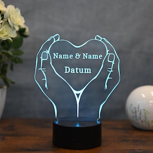 Peut inclure: Une veilleuse 3D imprimée en bleu en forme de deux mains tenant un cœur. Le cœur contient le texte "Name & Name Datum".