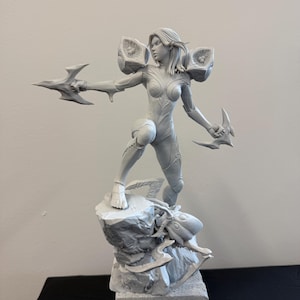 Puede incluir: Una figura gris de una guerrera en una pose dinámica, sosteniendo dos armas estilizadas. La figura está de pie sobre una base rocosa, con armadura detallada y cabello suelto. La escultura tiene una estética futurista.