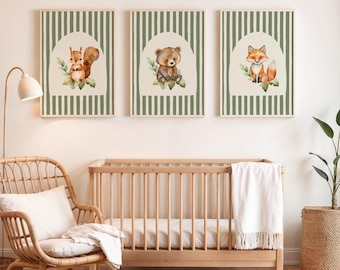 May include: Three framed art prints with watercolour illustrations of a squirrel, a bear, and a fox. Each animal is set against a cream background within a green striped frame. The prints are displayed above a wooden cot.