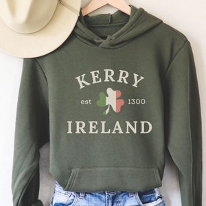 Op de afbeelding: Groen hoodie met de tekst "Kerry est 1300 Ireland" en een klavertjevier met de kleuren van de Ierse vlag.
