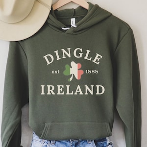 May include: Green hooded sweatshirt with a white graphic that says "Dingle, est 1585, Ireland" with a shamrock in the center. The shamrock is green, white, and orange.