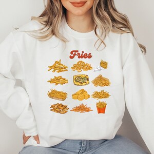 Pu&ograve; includere: Felpa bianca con la parola "Fries" in lettere rosse e una variet&agrave; di patatine fritte illustrate in giallo e marrone.