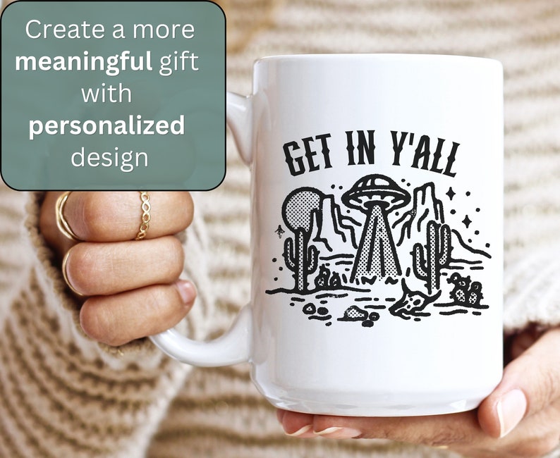 May include: White ceramic mug with a black and white illustration of a UFO over a desert landscape. The text "GET IN Y'ALL" is printed on the mug.