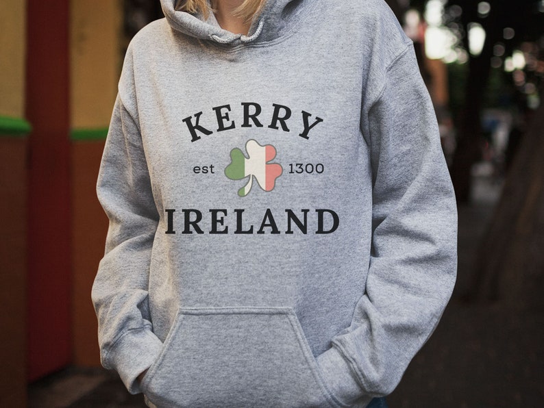 Op de afbeelding: Grijs hoodie met de tekst "Kerry est 1300 Ierland" en een groene klaver met oranje en witte accenten.
