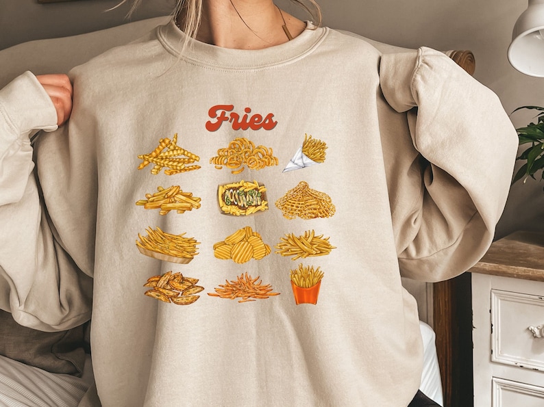 Pu&ograve; includere: Una felpa beige con la parola "Fries" stampata in rosso sul davanti. La felpa presenta una variet&agrave; di diversi tipi di patatine fritte, tra cui patatine fritte ricce, patatine fritte a cialde e patatine fritte francesi.