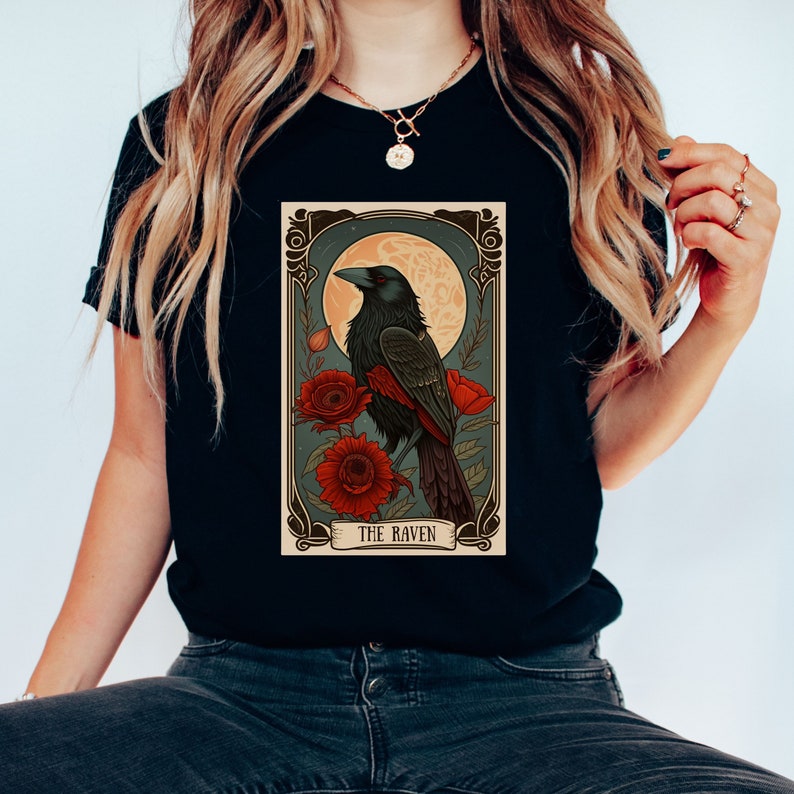 May include: Black t-shirt with a vintage tarot card design featuring a raven perched on a branch with red flowers and a full moon in the background. The card reads "The Raven".