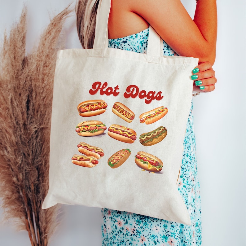 May include: A white canvas tote bag with the text "Hot Dogs" in red cursive lettering. The bag features a colorful illustration of various hot dogs with mustard, ketchup, and relish.