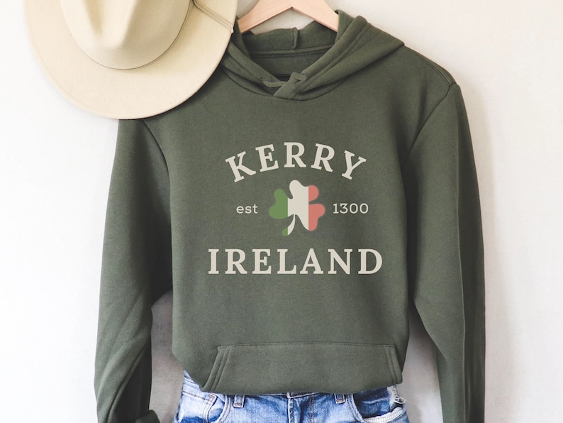 Op de afbeelding: Groen hoodie met de tekst "Kerry est 1300 Ireland" en een klavertjevier met de kleuren van de Ierse vlag.