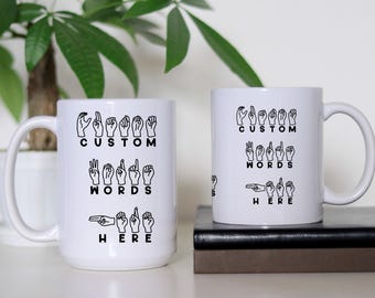 Pode incluir: Duas canecas de cerâmica branca com texto e imagens pretas. As canecas apresentam o texto "Custom Words Here" e imagens de mãos assinando as letras do alfabeto.