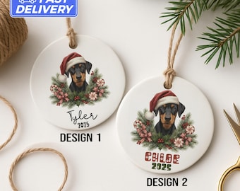 May include: Two white ceramic Christmas ornaments featuring a Doberman Pinscher wearing a Santa hat. Design 1 has the name "Tyler" and "2025". Design 2 has the name "Chloe" and "2025". Both designs have a festive wreath.