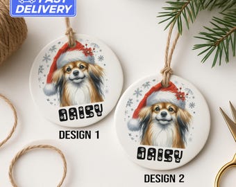 May include: Two round ceramic Christmas ornaments featuring a dog wearing a Santa hat. The dog has brown and white fur. The name "DAISY" is printed below the dog's image, with paw prints in the letters. Design 1 and Design 2 are labeled.