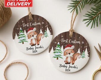 May include: Two circular Christmas decorations with a wood-effect background. Each features a cartoon fox in a Santa hat, with snowy trees. The text "First Custom" and "Baby Jacob's 2024" are printed on the ornaments, with a twine loop for hanging.