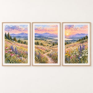 Könnte beinhalten: Ein Set aus drei vertikalen gerahmten Wandbildern mit einer durchgehenden Aquarell-Landschaft aus einer Wildblumenwiese, sanften Hügeln und fernen Bergen unter einem weichen, rosa und orangefarbenen Sonnenuntergangshimmel.