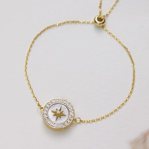 May include: A gold chain bracelet with a white and gold star charm. The bracelet has an adjustable sliding clasp.