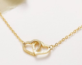 May include: A gold necklace with a delicate chain and a double heart pendant. The hearts are intertwined and have a textured surface.