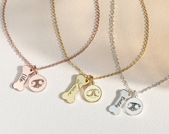 Pode incluir: Três colares de ouro, prata e ouro rosa com pingentes em forma de osso e pingentes redondos gravados. Os pingentes são gravados com os nomes "Lila", "Jasper" e "Buddy".