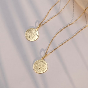 Puede incluir: Dos collares de oro con colgantes circulares. Un colgante presenta un diseño de cangrejo estilizado con un pequeño diamante en el centro. El otro colgante presenta una cara estilizada con una corona y estrellas.