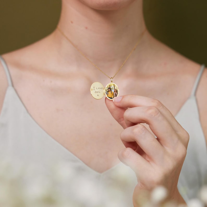 Op de afbeelding: Een gouden ovale ketting met een hanger waarin een foto zit. De achterkant van de hanger is gegraveerd met de boodschap "Ik hou van je" en een hart.