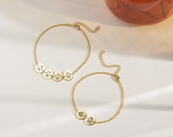 May include: Two gold chain bracelets with paw print charms. The larger bracelet has four charms and the smaller bracelet has two charms.